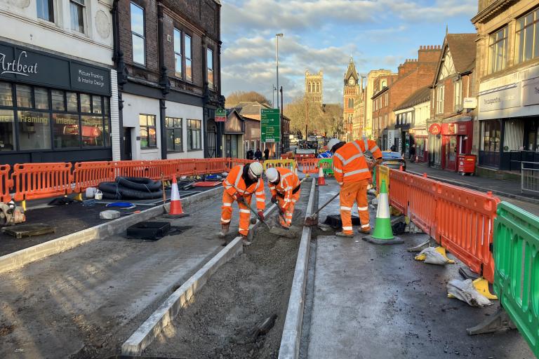 Highways workers in orange hi-vis, working on the construction of a cycleway, closed off with orange barriers.