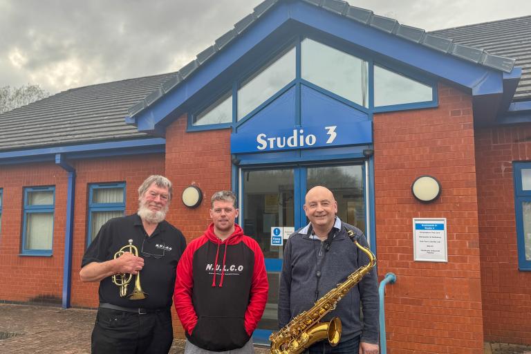 Three men standing in front of a studio unit at Silverdale Enterprise Centre. The first man is holding a trumpet and the third man is holding a saxophone.
