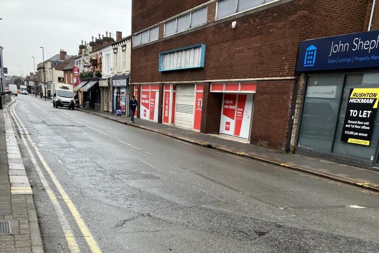 A surface-worn road in Burton town centre, with businesses running along the right side of the road.