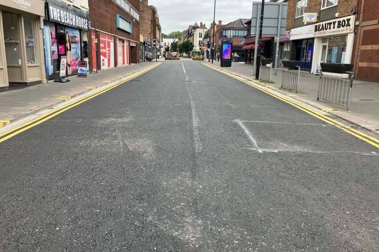 A smooth and freshly resurfaced road with bold double yellow painted lines either side and businesses lining the road on both sides.