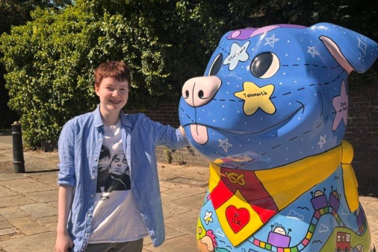 A young woman standing next to a giant colourful Staffordshire Bull Terrier sculpture.