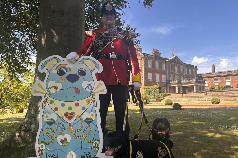 Two Staffordshire bull terriers and their handler in red uniform standing next to a cutout of 'Staffy', the county's new Staffordshire Bull Terrier tourism mascot.