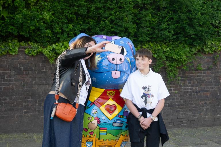 A woman taking a selfie with her son in front of a large and colourful Staffordshire Bull Terrier sculpture.