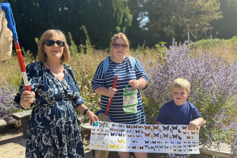 Janet Higgins holding up poster of butterflies with young boy Isaac and his mum Emily in the countryside