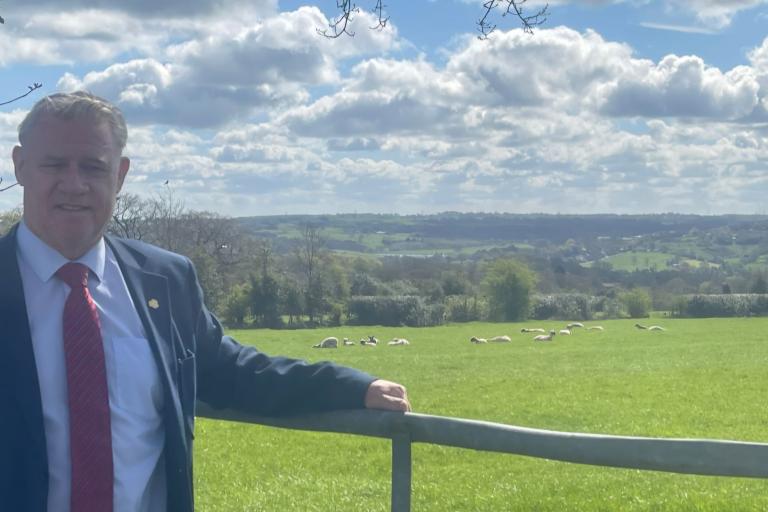 Anthony screen in the countryside, leaning on a fence with a field and sheep behind him