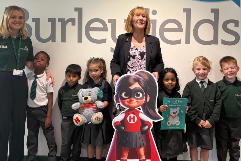 School pupils and staff with a Little Heroes character, teddy bear and wellbeing book at Burleyfields Primary School.