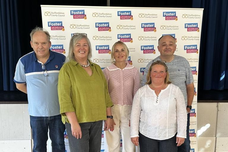 Foster carers stood in front of promotional banner