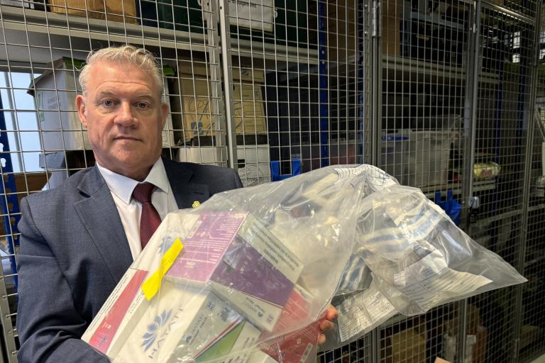Anthony Screen holding bags of seized products inside a secure storage area with metal cages and shelving in the background.