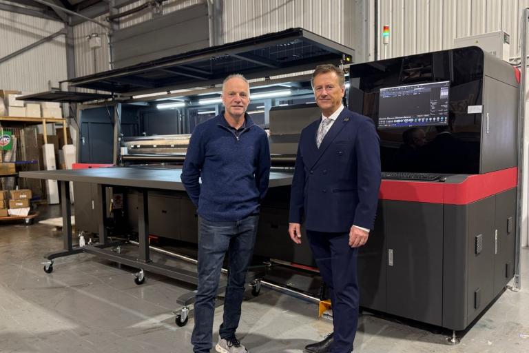 Two smartly dressed men standing in front of a large industrial printer.