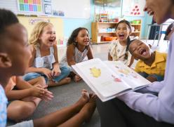 children sat around an adult who is reading a book