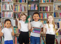 Four children standing in front of bookshelves, each holding books and smiling.