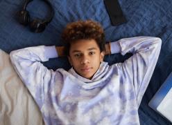 Youthful serene boy in stylish hoodie looking at camera while lying on bed