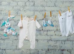 Children's white bodysuit, boots and a toy rabbit dry on a rope against a white brick wall