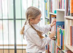 A young girl choosing a book to read from a bookshelf filled with books