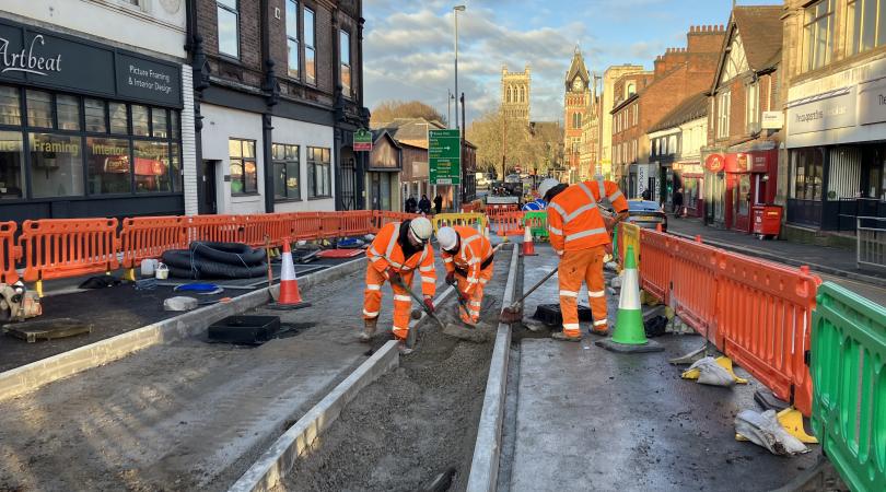 Highways workers in orange hi-vis, working on the construction of a cycleway, closed off with orange barriers.