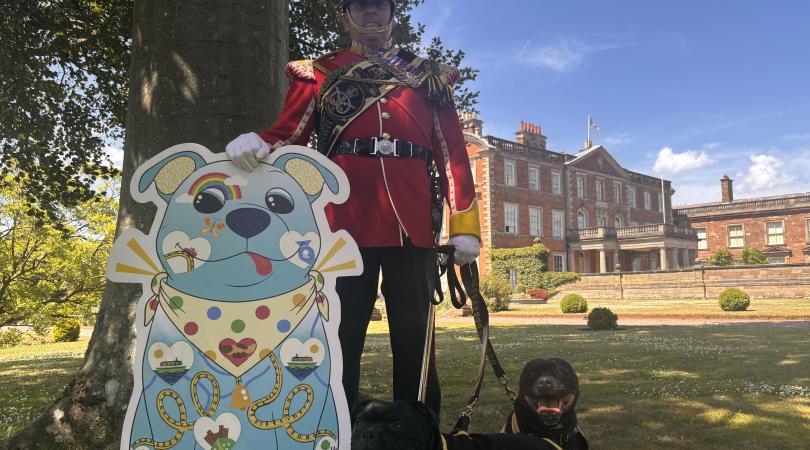 Two Staffordshire bull terriers and their handler in red uniform standing next to a cutout of 'Staffy', the county's new Staffordshire Bull Terrier tourism mascot.