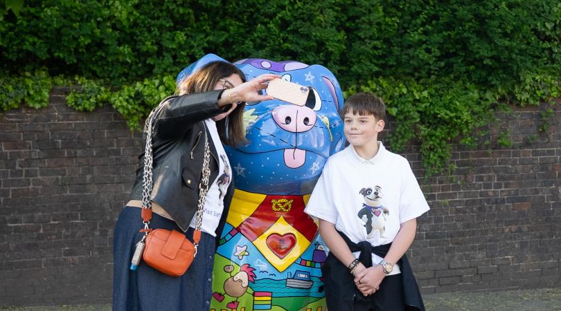A woman taking a selfie with her son in front of a large and colourful Staffordshire Bull Terrier sculpture.