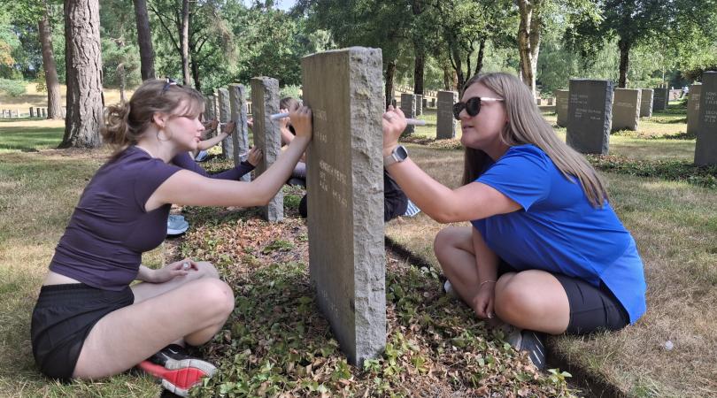 Teenagers tending to graves with trees surrounding them