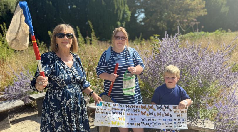 Janet Higgins holding up poster of butterflies with young boy Isaac and his mum Emily in the countryside