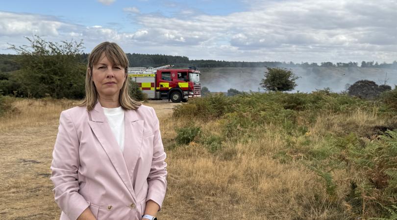 Councillor Hayley Coles standing in front of smoking heathlands at Cannock Chase, with fire engine to her left