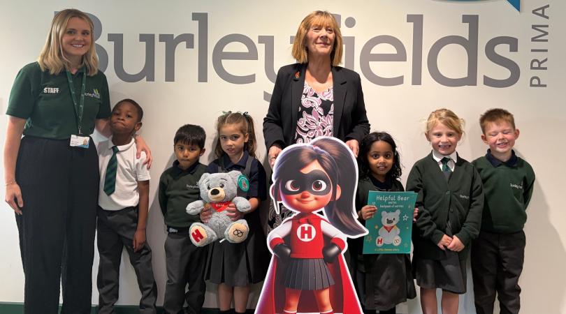School pupils and staff with a Little Heroes character, teddy bear and wellbeing book at Burleyfields Primary School.