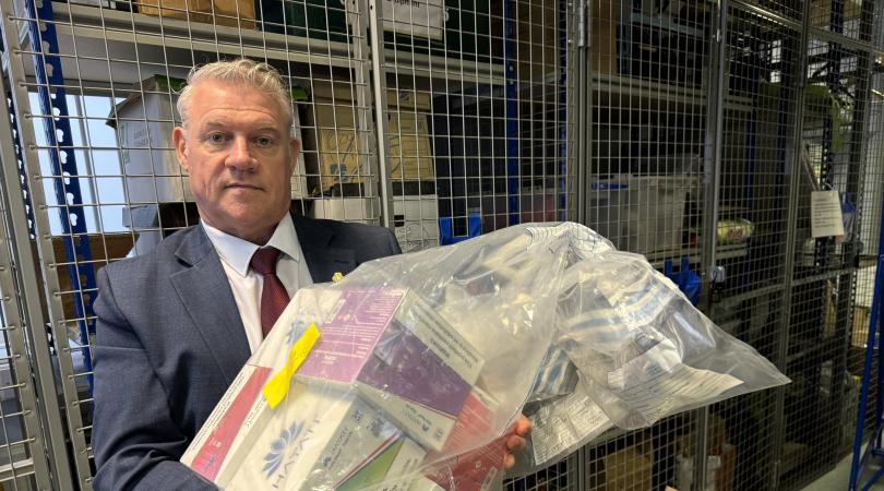 Anthony Screen holding bags of seized products inside a secure storage area with metal cages and shelving in the background.